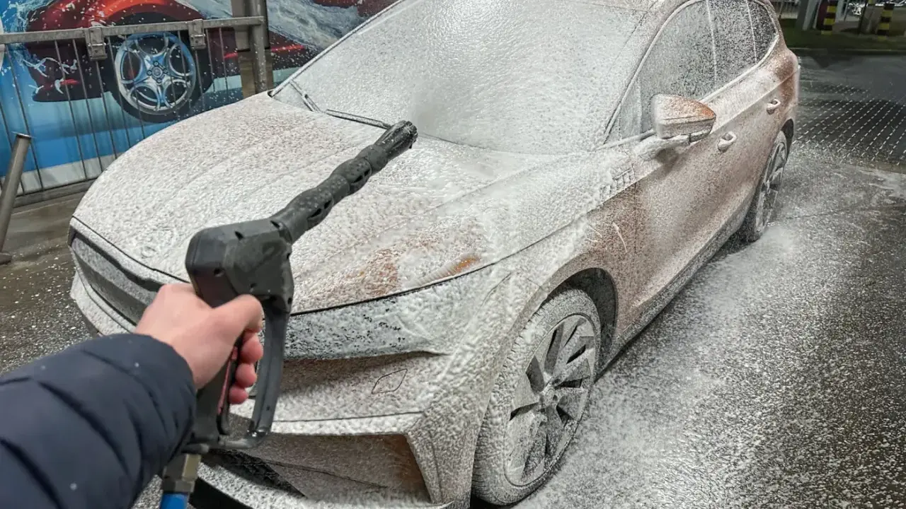 Jak myć auto na myjni: piana pokrywa samochód, a ręka trzyma pistolet ciśnieniowy.