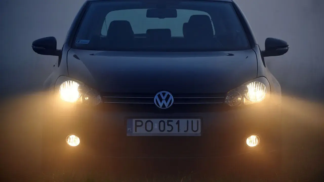Ciemny Volkswagen z włączonymi światłami przeciwmgielnymi przednimi, poprawiającymi widoczność w mgle.
