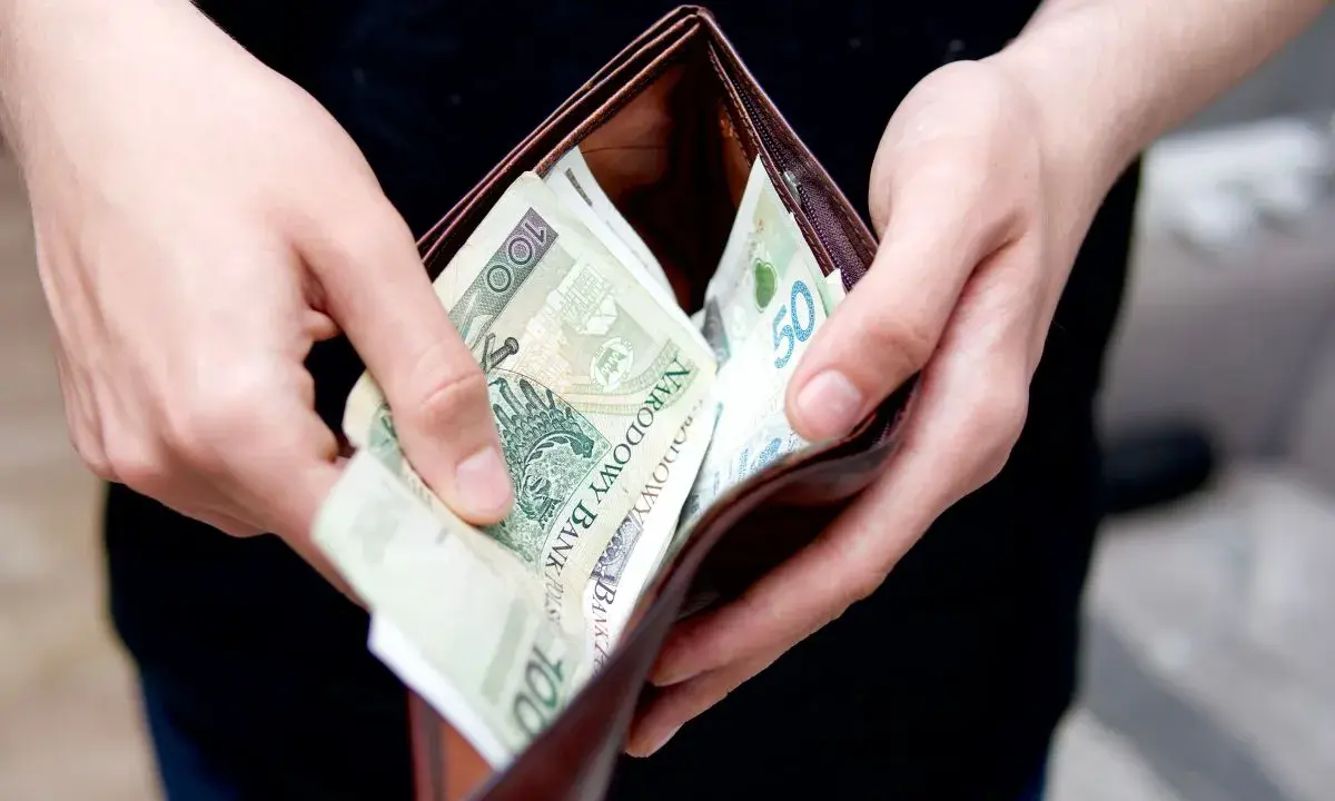 Ręce trzymają portfel z polskimi banknotami. Zastanawiasz się, ile kosztuje przegląd samochodu z gazem?