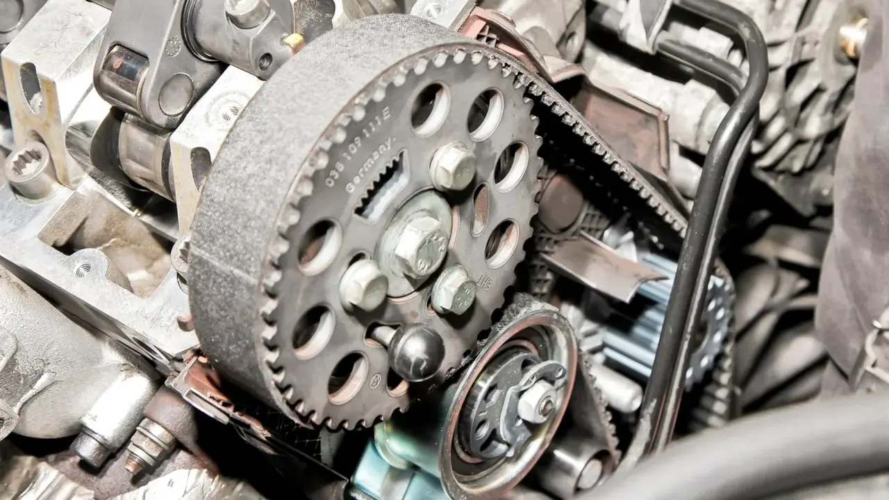 Zbliżenie na mechanizm rozrządu silnika, widoczny jest czujnik położenia wałka rozrządu, koło pasowe i pasek.