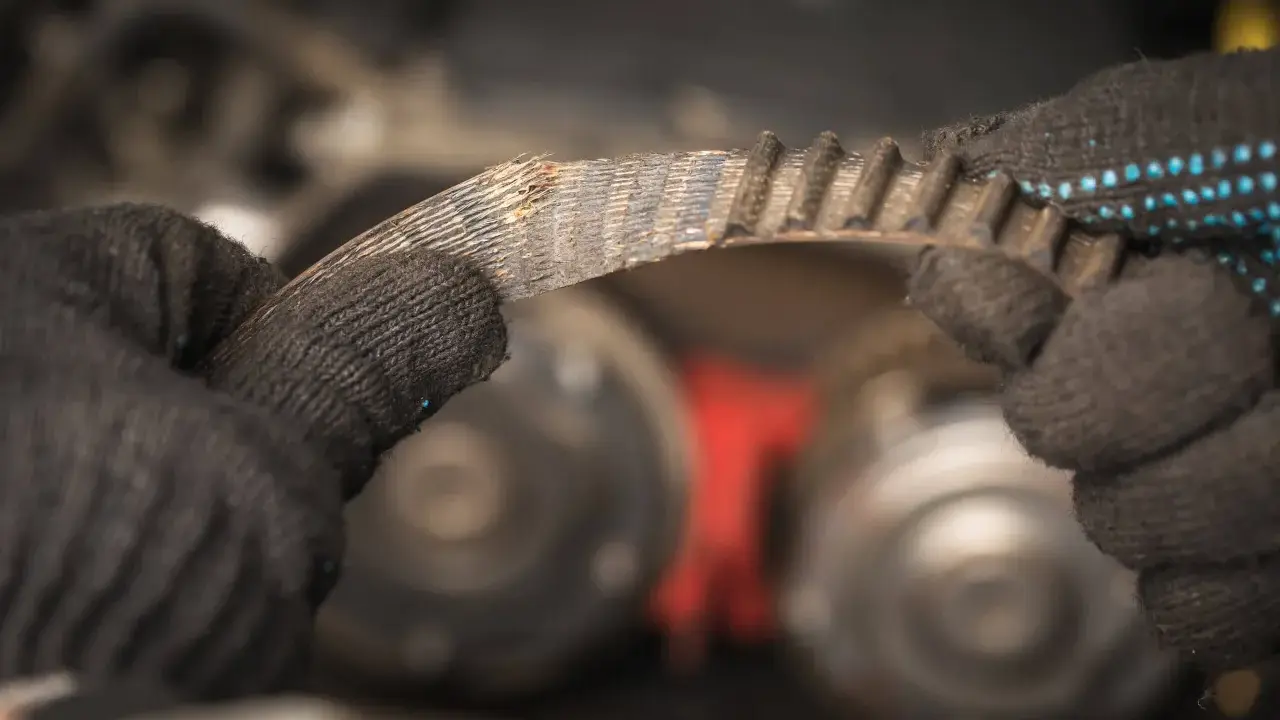 Zużyty pasek klinowy w rękach mechanika, przygotowanie do wymiany.