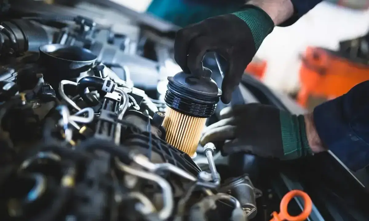 Mechanik w czarnych rękawiczkach dokonuje wymiany filtra paliwa w silniku samochodowym.