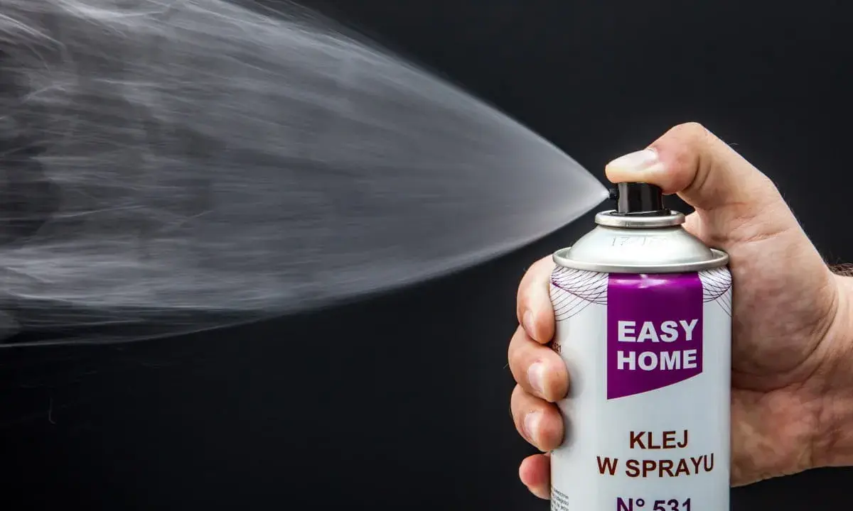 Dłoń trzyma puszkę z napisem "EASY HOME KLEJ W SPRAYU", rozpylając białą mgiełkę. Idealny klej do podsufitki bez zdejmowania.