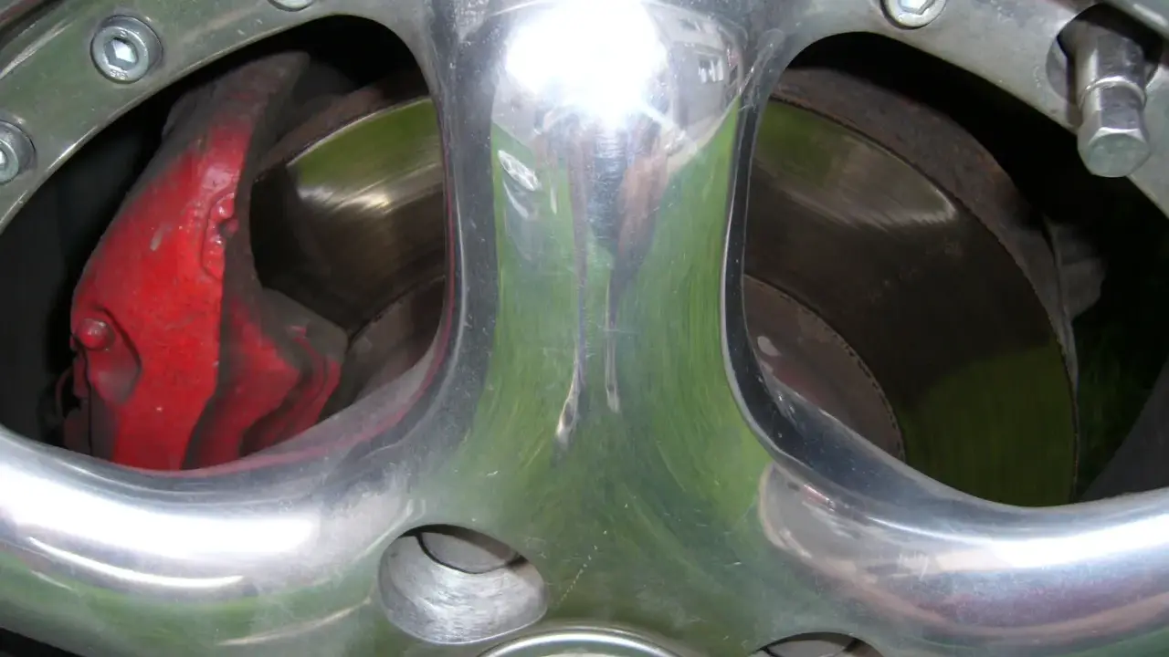Błyszczące polerowanie aluminium felgi z widocznym czerwonym zaciskiem hamulcowym i tarczą.