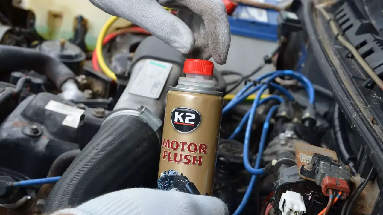 Ręka w rękawiczce trzyma puszkę K2 Motor Flush, najlepsza płukanka do silnika benzynowego, gotowa do użycia w samochodzie.