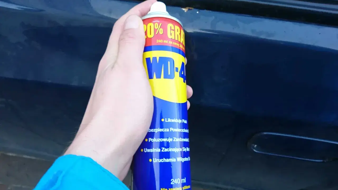 Dłoń trzyma puszkę WD-40, gotową do usuwania rdzy z samochodu.