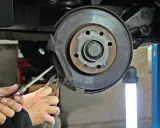 Mechanik wymienia klocki hamulcowe. Widać zużyte tarcze hamulcowe i narzędzia.