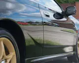 Błyszczący czarny lakier samochodu odbija chmury i inne pojazdy, tworząc efektowne hologramy na lakierze.