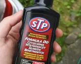 Dłoń trzyma butelkę STP z formułą do czyszczenia wtryskiwaczy silników benzynowych.