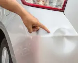 Dłoń wskazuje na wgniecenia na srebrnym samochodzie. Sprawdź wyciąganie wgniotek cena.