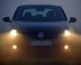 Ciemny Volkswagen z włączonymi światłami przeciwmgielnymi przednimi, poprawiającymi widoczność w mgle.