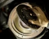 Dłoń trzymająca tarczę sprzęgła nad mechanizmem w samochodzie.