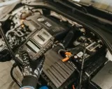 Mechanik w rękawiczkach trzyma tester akumulatora, który może zawierać czujnik Halla, sprawdzając stan pojazdu.