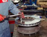 Mechanik w czerwonych rękawicach dokręca śruby nowej tarczy hamulcowej. Pytanie: co ile wymiana tarcz hamulcowych?