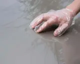 Dłoń w rękawiczce ochronnej dotyka lśniącego, szarego lakieru samochodowego.