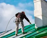 Pracownik na dachu maluje pistoletem zielony dach. Czy Hammerite można malować pistoletem? Tak, można!