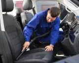 Mężczyzna w niebieskim kombinezonie odkurza siedzenie samochodu z alcantarą, dbając o każdy detal.
