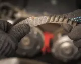 Zużyty pasek klinowy w rękach mechanika, przygotowanie do wymiany.