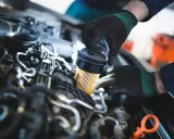 Mechanik w czarnych rękawiczkach dokonuje wymiany filtra paliwa w silniku samochodowym.