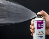 Dłoń trzyma puszkę z napisem "EASY HOME KLEJ W SPRAYU", rozpylając białą mgiełkę. Idealny klej do podsufitki bez zdejmowania.