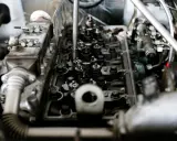Widok wnętrza silnika z widocznymi zaworami i sprężynami. Widać fragmenty układu paliwowego i metalowe elementy, które są częścią mechanizmu, gdzie pracują tłoki.