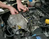 Ręce mechanika pracujące przy silniku samochodowym, widoczne elementy układu paliwowego i czujnik.