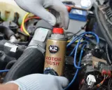 Ręka w rękawiczce trzyma puszkę K2 Motor Flush, najlepsza płukanka do silnika benzynowego, gotowa do użycia w samochodzie.