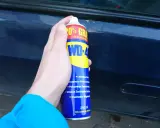 Dłoń trzyma puszkę WD-40, gotową do usuwania rdzy z samochodu.