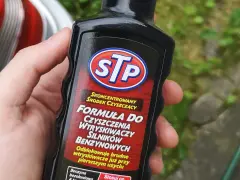 Dłoń trzyma butelkę STP z formułą do czyszczenia wtryskiwaczy silników benzynowych.
