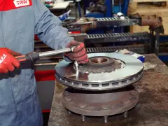 Mechanik w czerwonych rękawicach dokręca śruby nowej tarczy hamulcowej. Pytanie: co ile wymiana tarcz hamulcowych?