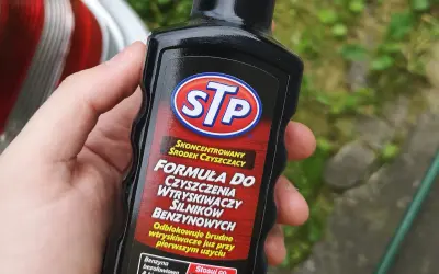 Dłoń trzyma butelkę STP z formułą do czyszczenia wtryskiwaczy silników benzynowych.
