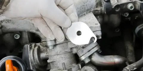 Ręka w białej rękawiczce trzyma metalową płytkę do zaslepienia EGR.