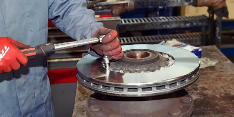 Mechanik w czerwonych rękawicach dokręca śruby nowej tarczy hamulcowej. Pytanie: co ile wymiana tarcz hamulcowych?