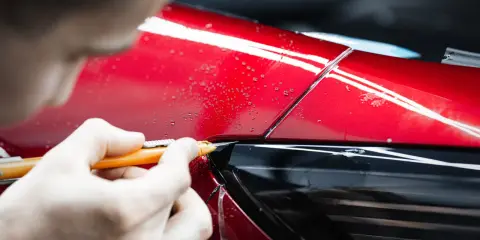 Precyzyjne cięcie folii PPF na czerwonym błyszczącym lakierze samochodu.