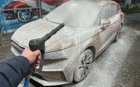 Jak myć auto na myjni: piana pokrywa samochód, a ręka trzyma pistolet ciśnieniowy.