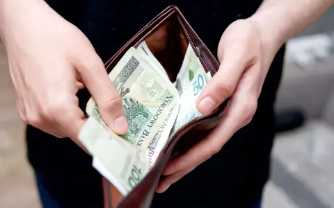 Ręce trzymają portfel z polskimi banknotami. Zastanawiasz się, ile kosztuje przegląd samochodu z gazem?