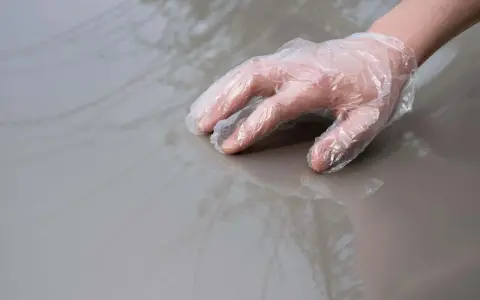 Dłoń w rękawiczce ochronnej dotyka lśniącego, szarego lakieru samochodowego.