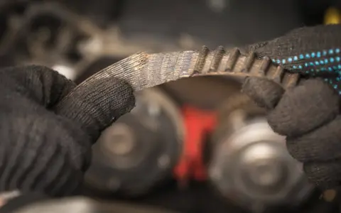 Zużyty pasek klinowy w rękach mechanika, przygotowanie do wymiany.