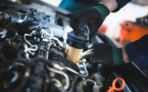 Mechanik w czarnych rękawiczkach dokonuje wymiany filtra paliwa w silniku samochodowym.