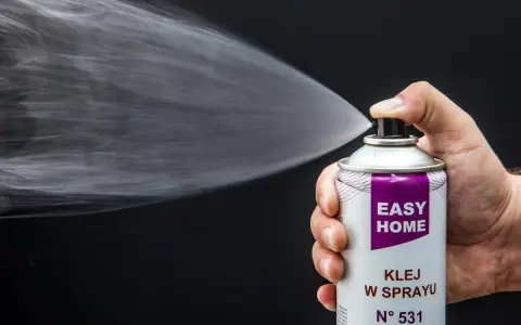 Dłoń trzyma puszkę z napisem "EASY HOME KLEJ W SPRAYU", rozpylając białą mgiełkę. Idealny klej do podsufitki bez zdejmowania.