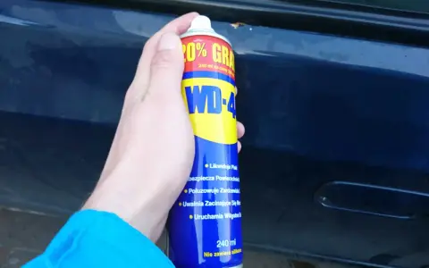 Dłoń trzyma puszkę WD-40, gotową do usuwania rdzy z samochodu.