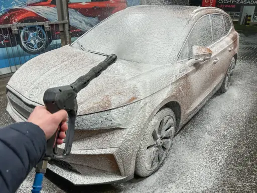 Jak myć auto na myjni: piana pokrywa samochód, a ręka trzyma pistolet ciśnieniowy.