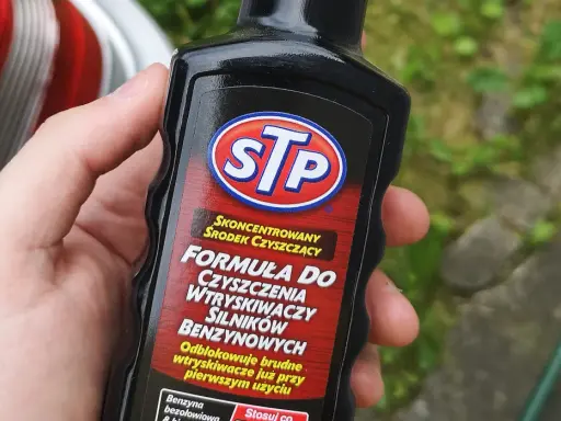 Dłoń trzyma butelkę STP z formułą do czyszczenia wtryskiwaczy silników benzynowych.
