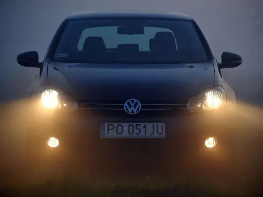 Ciemny Volkswagen z włączonymi światłami przeciwmgielnymi przednimi, poprawiającymi widoczność w mgle.
