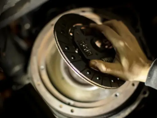 Dłoń trzymająca tarczę sprzęgła nad mechanizmem w samochodzie.