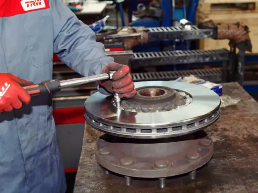 Mechanik w czerwonych rękawicach dokręca śruby nowej tarczy hamulcowej. Pytanie: co ile wymiana tarcz hamulcowych?
