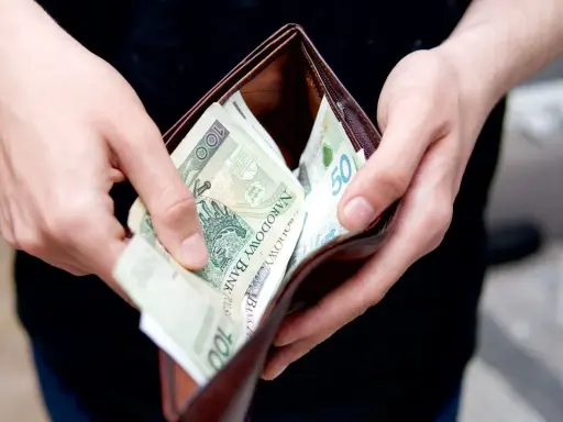Ręce trzymają portfel z polskimi banknotami. Zastanawiasz się, ile kosztuje przegląd samochodu z gazem?