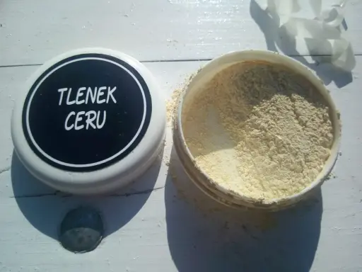 Otwarty pojemnik z jasnym proszkiem, na wieczku napis "TLENEK CERU".