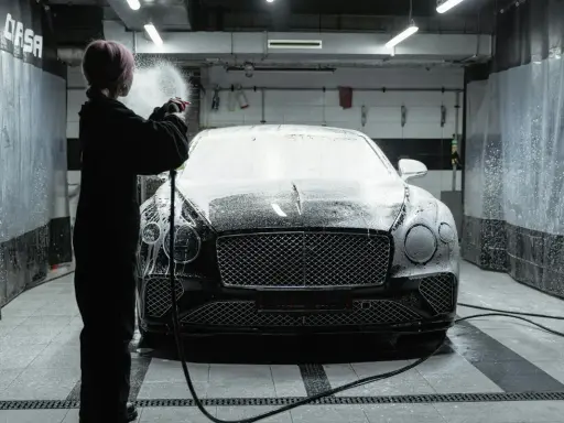 Osoba w czarnym kombinezonie spryskuje czarnego Bentleya pianą w myjni. Detailing co to? To dbałość o każdy szczegół luksusowego auta.