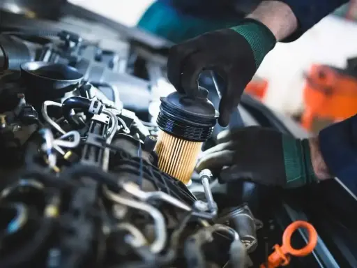 Mechanik w czarnych rękawiczkach dokonuje wymiany filtra paliwa w silniku samochodowym.